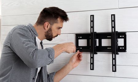 A person levelling and fixing a TV wall mounting plate to the wall